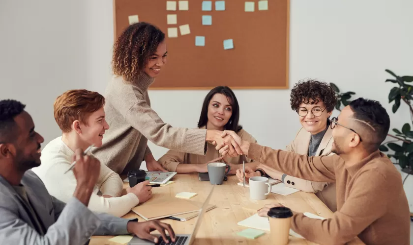 Een groep mensen die rond de tafel zit en twee mensen schudden elkaar de hand